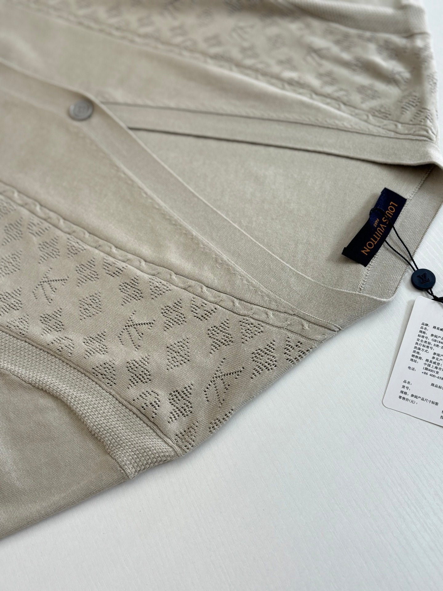 Beige cardigan front panel with patterned fabric, button detail, and hanging tag