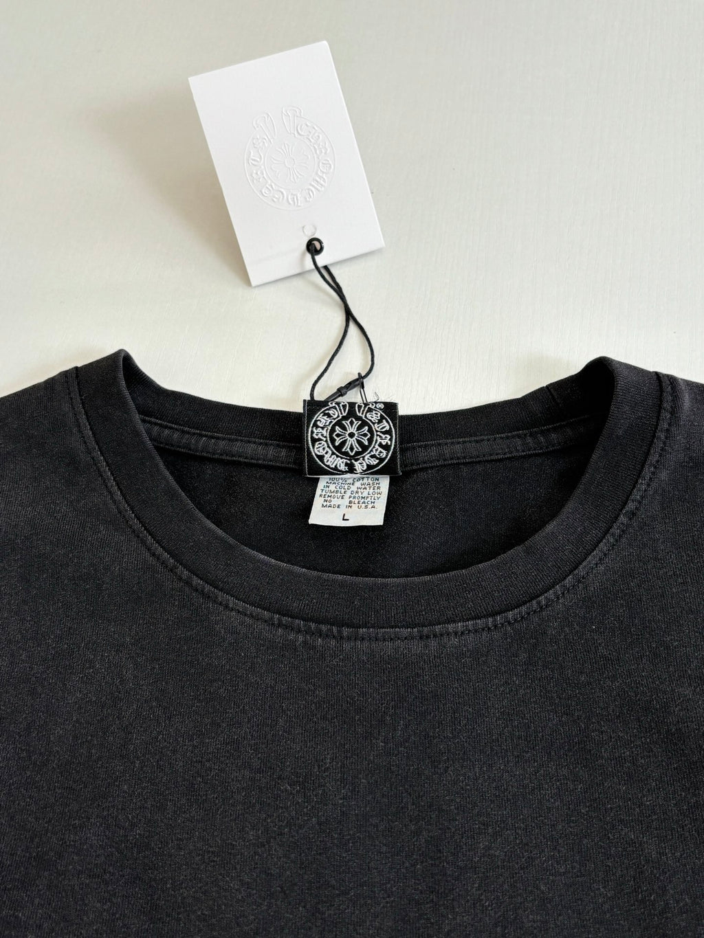 Dark crew-neck long-sleeve T-shirt with collar tag and small round chest logo