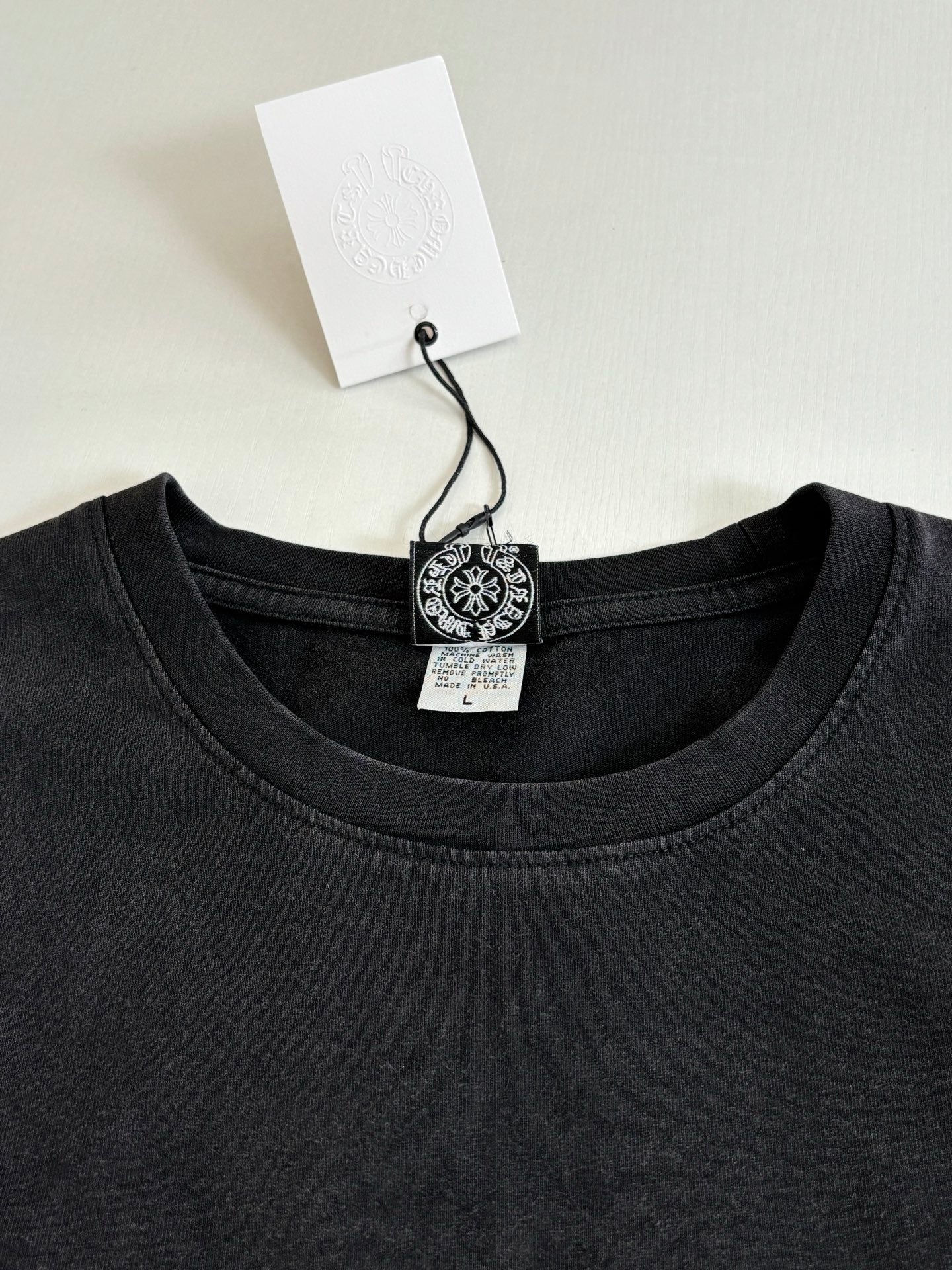 Dark crew-neck long-sleeve T-shirt with collar tag and small round chest logo