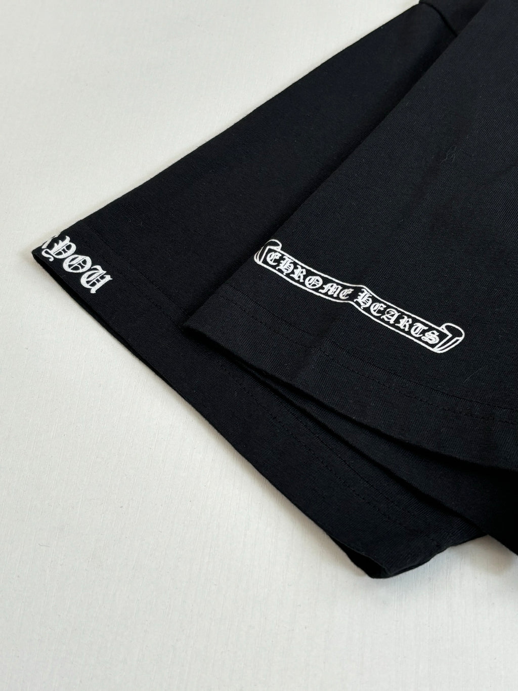 Black T-shirt sleeve close-up with small script logo printed near the hem