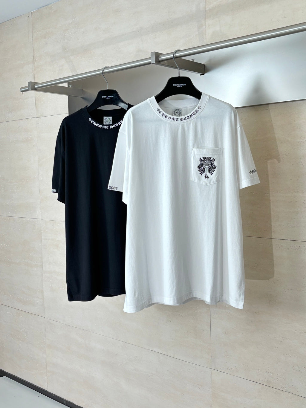 White crew-neck T-shirt with black front crest; black T-shirt beside it