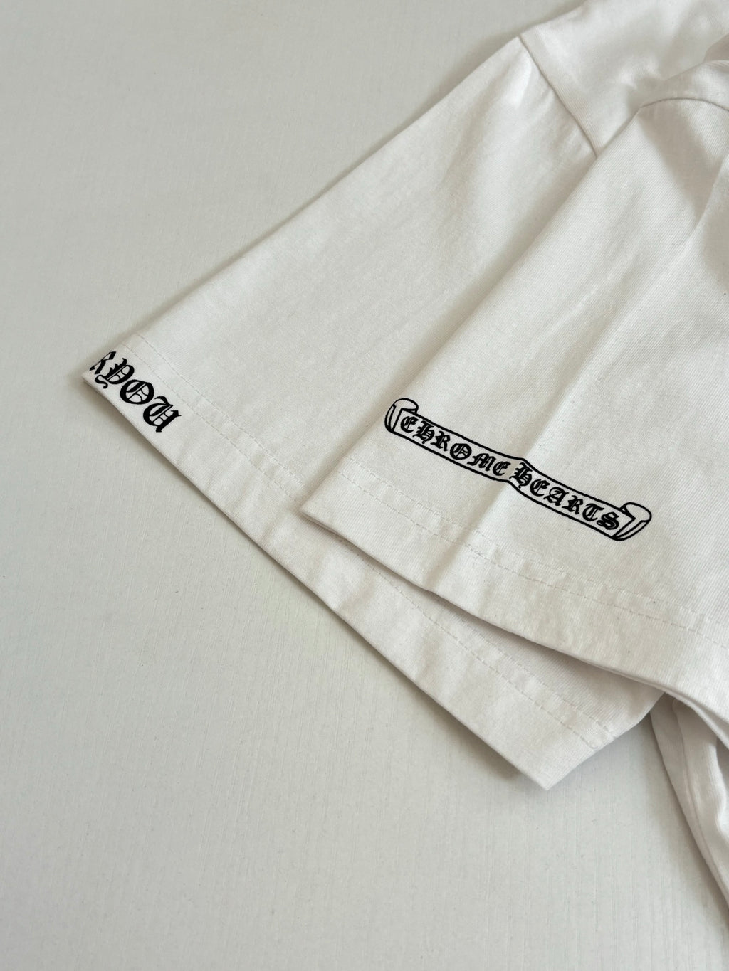 White T-shirt sleeve with small black Chrome Hearts text print