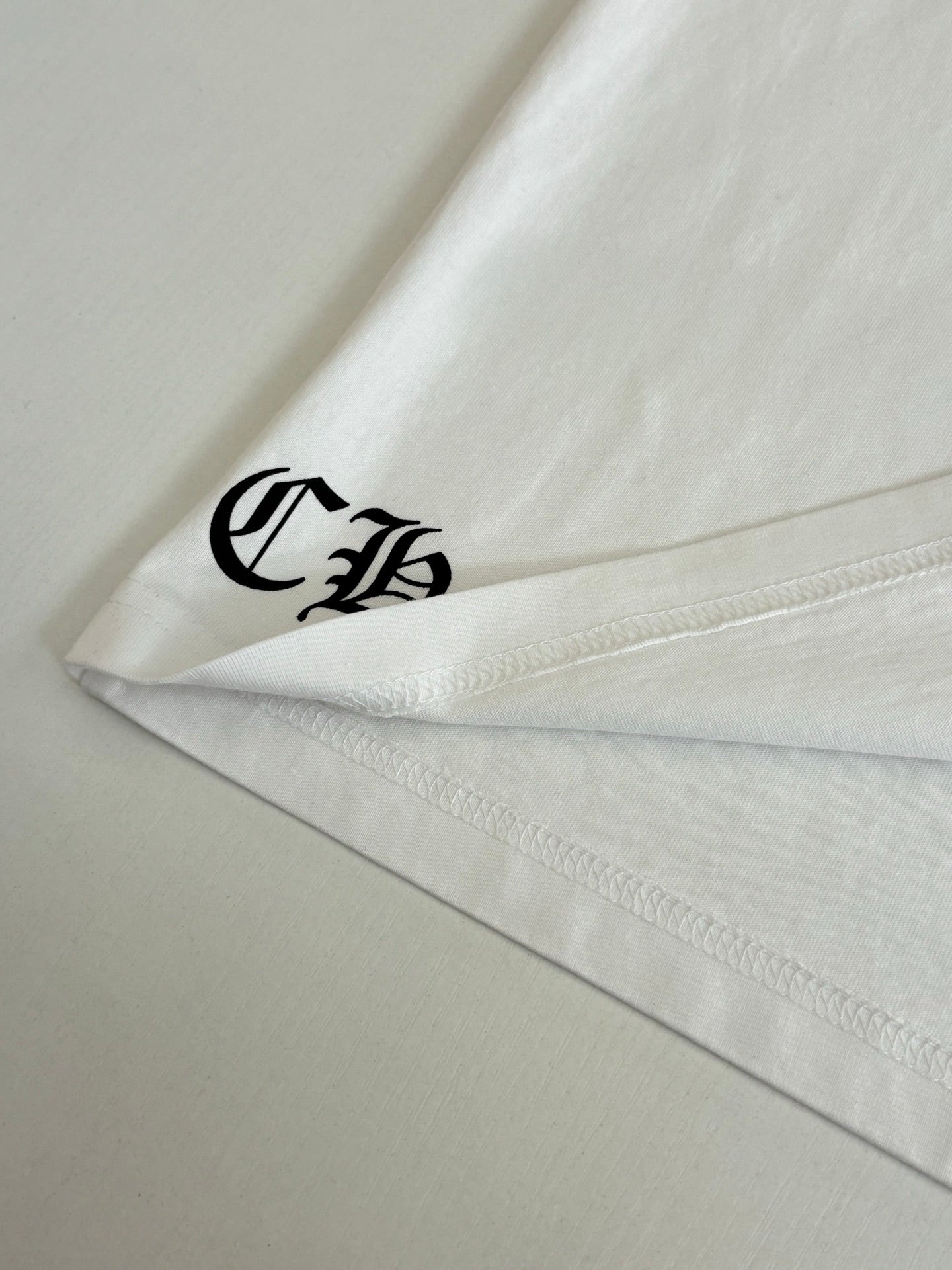 White T-shirt hem corner with small black logo print.