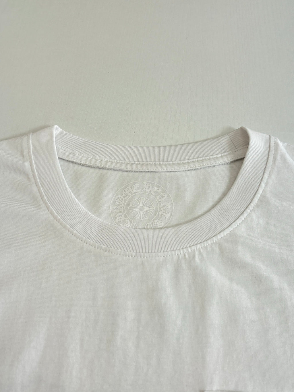 White crew-neck T-shirt neckline with subtle embossed logo detail.