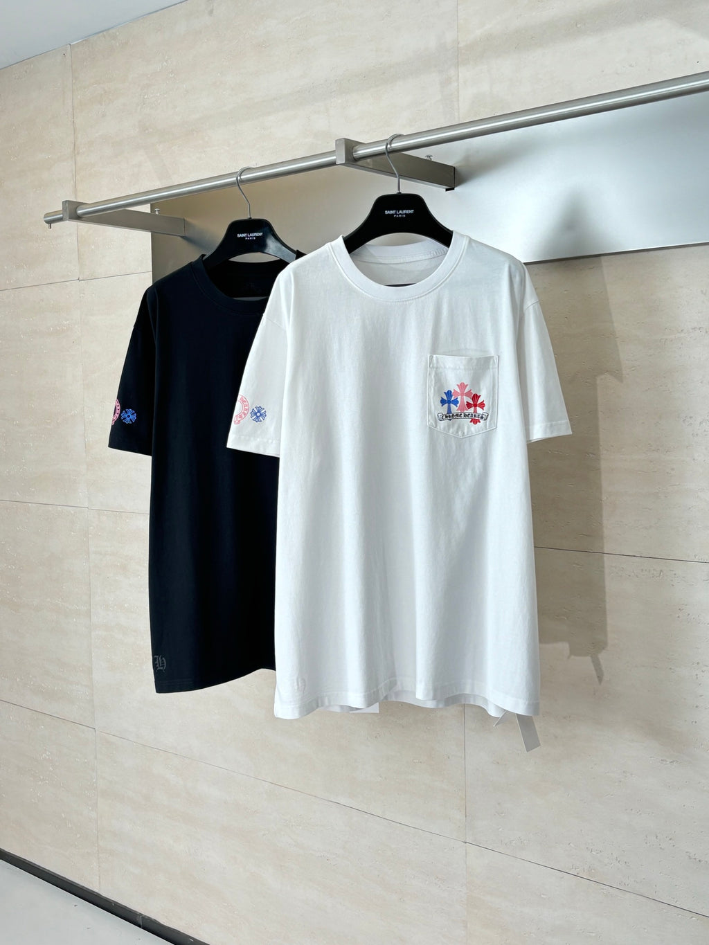 White and black short-sleeve T-shirts on hangers, each with multicolor logo accents.