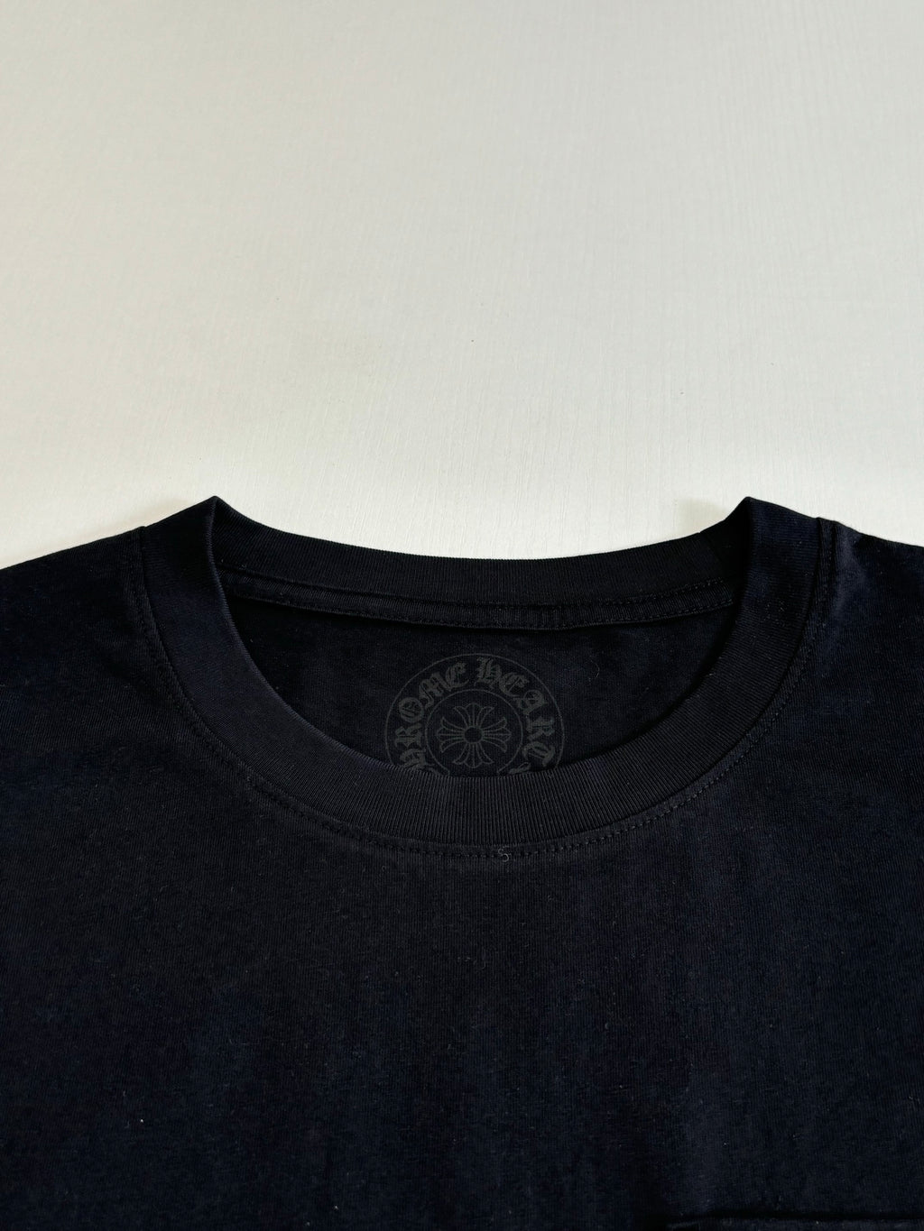 Black short-sleeve T-shirt neckline with circular embossed brand mark