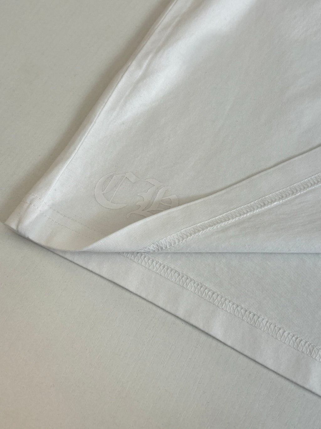 White T-shirt side seam with tonal embossed logo near the hem