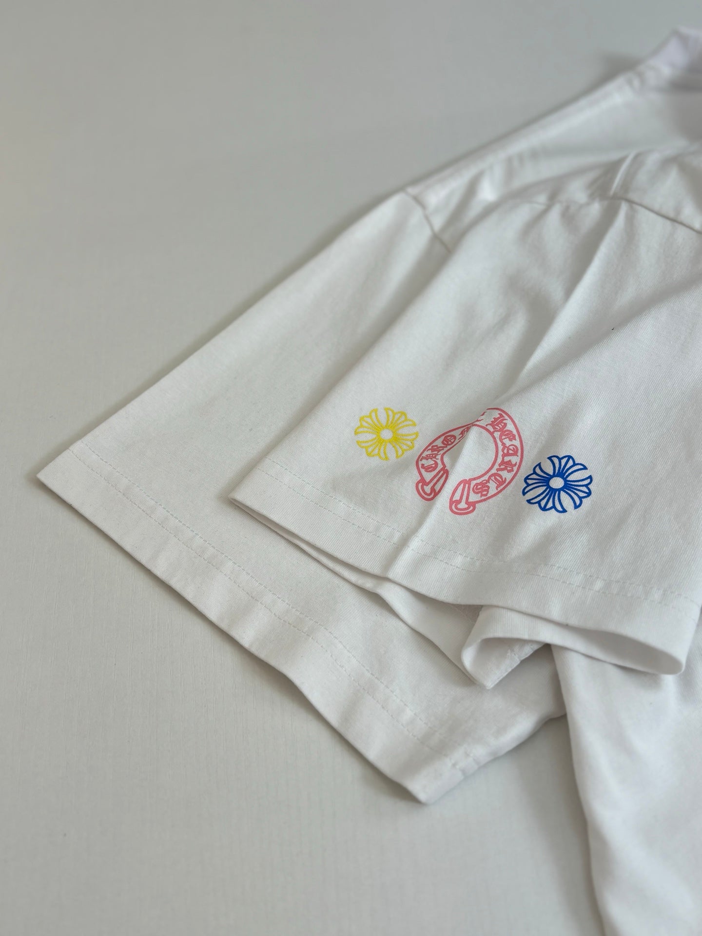White T-shirt sleeve and hem with small multicolor icon prints.
