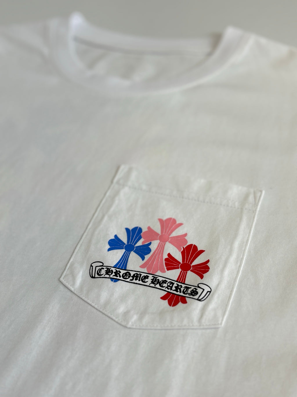 Patch-style graphic with red and blue flowers and outlined text on white T-shirt.