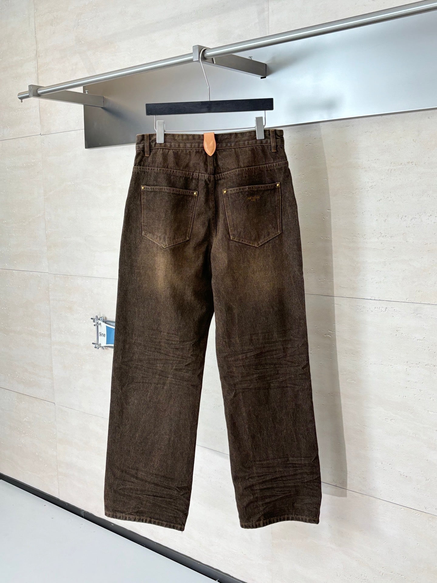 Brown denim pants on hanger, button waist, two front pockets, and belt loops.