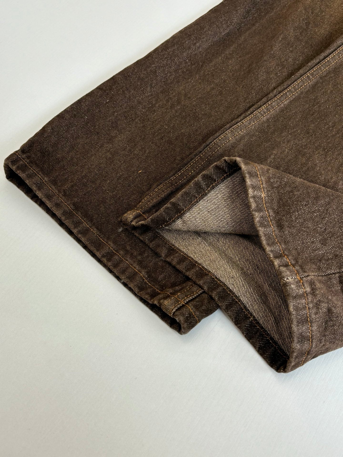 Brown denim pants hem with stitched cuff and folded leg opening detail.