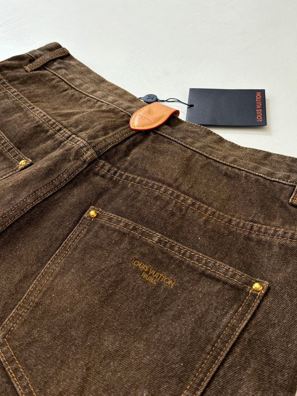 Brown denim pants with front pockets, stitched fly, and button closure
