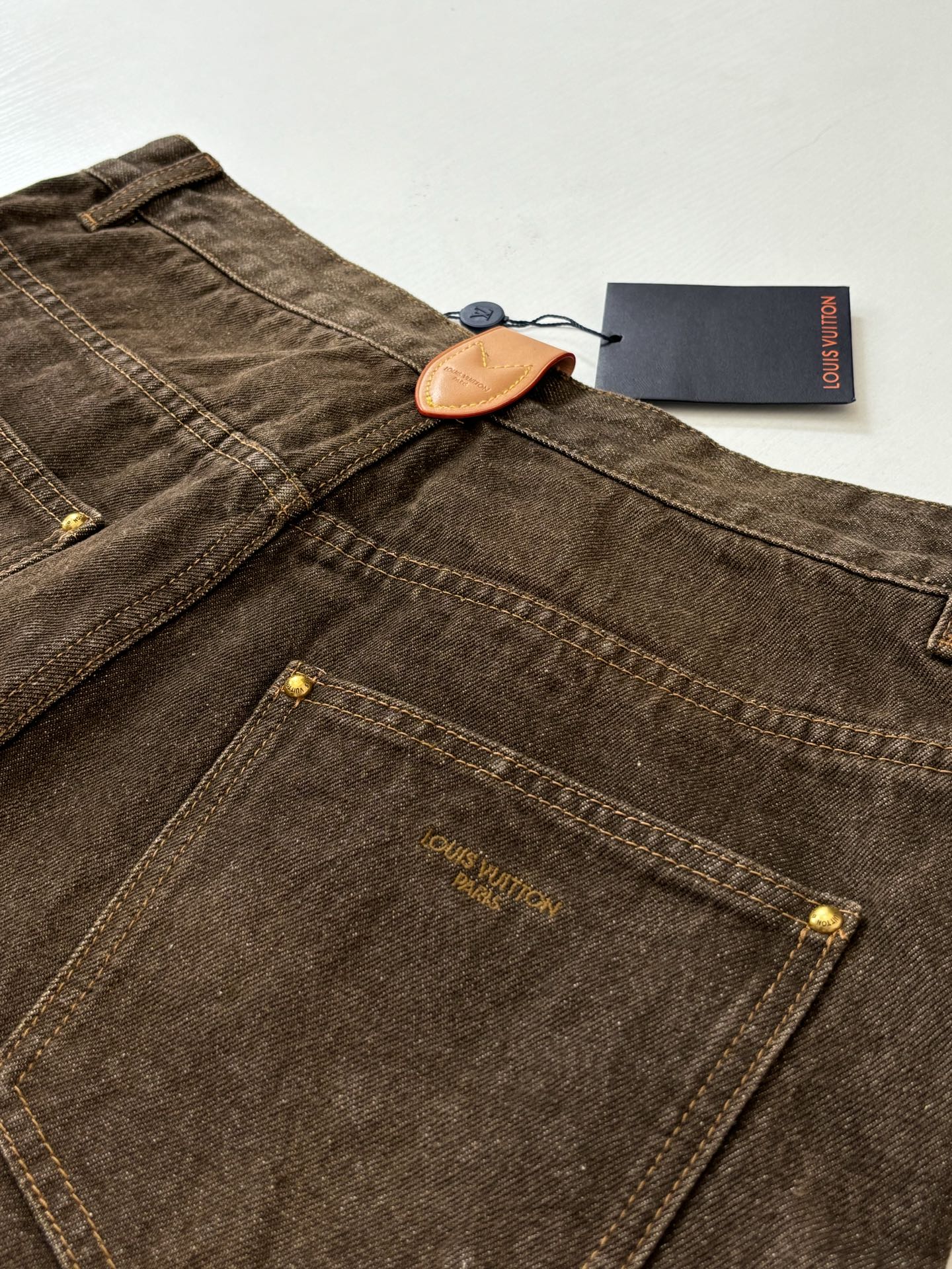Brown denim pants with front pockets and contrast stitching, gold-tone buttons