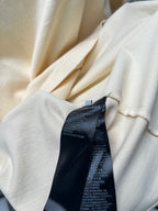 Cream T-shirt fabric close-up with black brand care label at collar seam.