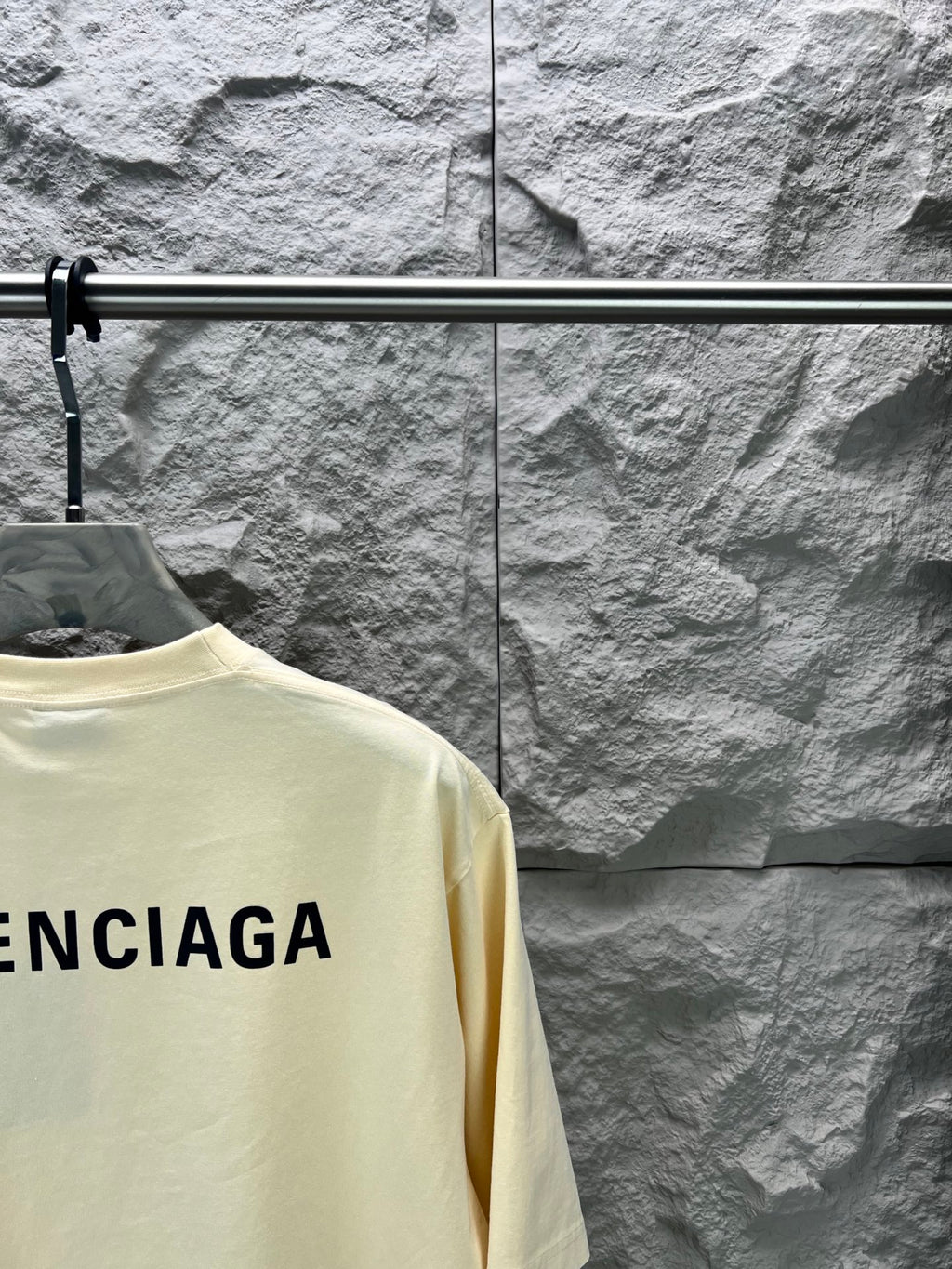 Cream short-sleeve T-shirt detail with partial BALENCIAGA logo on back.
