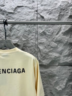 Cream short-sleeve T-shirt detail with partial BALENCIAGA logo on back.