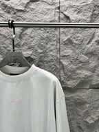 White T-shirt with small pink logo on chest, close-up