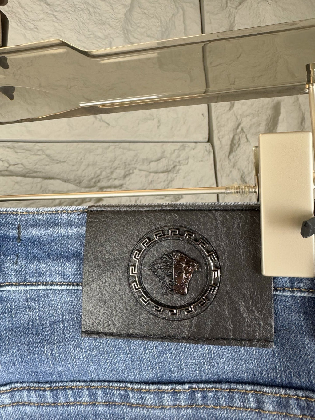 Versace denim jeans back waistband close-up with black logo patch and embossed emblem