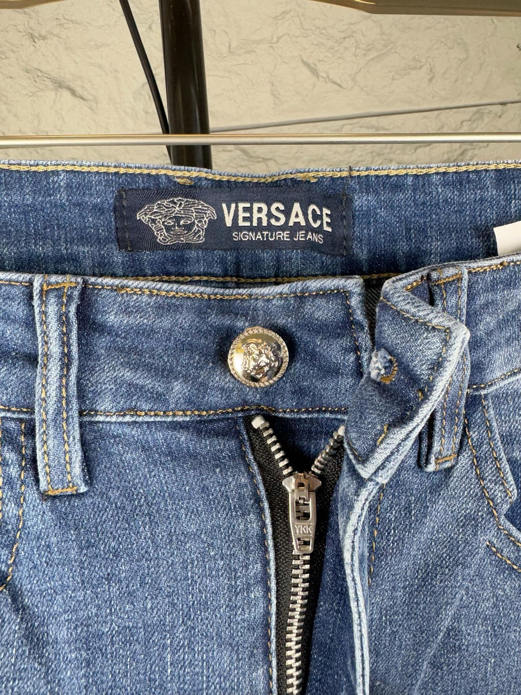 Versace denim jeans waistband close-up with VERSACE text logo and zipper fly