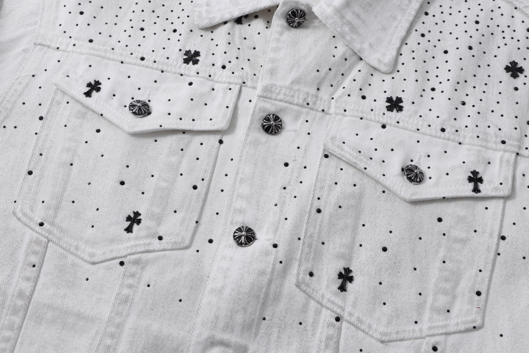 White denim jacket front with flap pockets, button placket, and embroidered cross and dot pattern