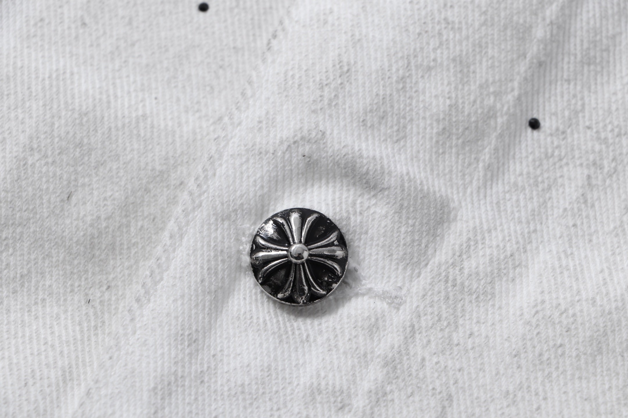 Dark metal button on white denim jacket with ridged floral design