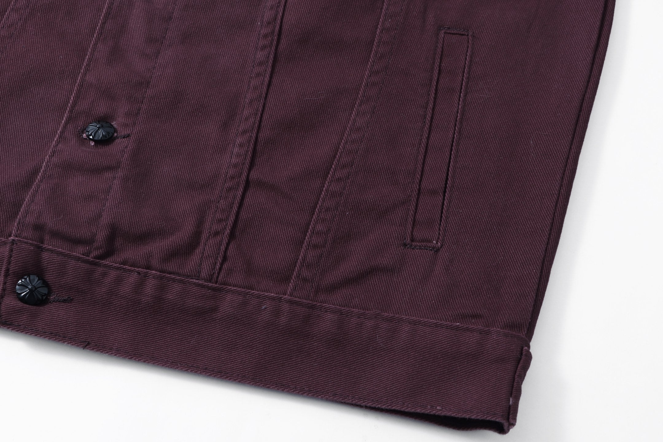 Lower front pocket seam and button detail on dark plum long-sleeve jacket
