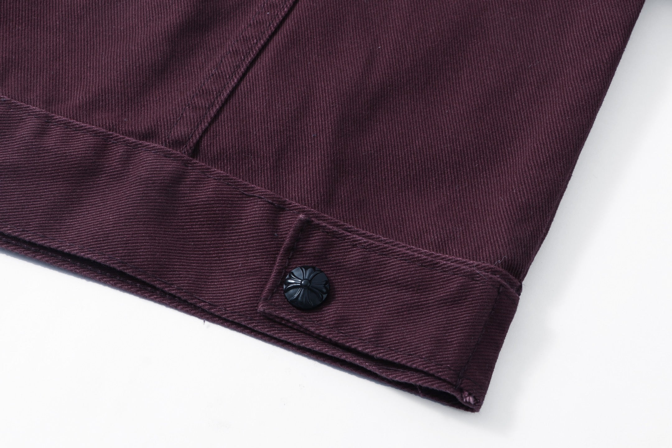 Cuffed hem corner detail on dark plum long-sleeve jacket with button fastening