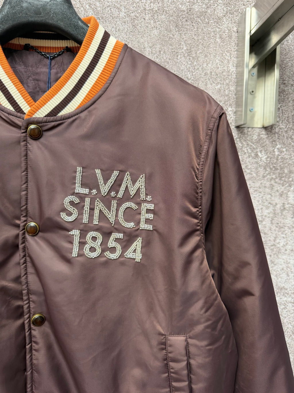 Louis Vuitton long bomber jacket close-up on chest logo reading LVM Since 1854