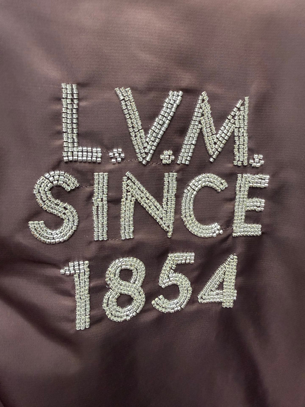Louis Vuitton long bomber jacket close-up of LVM Since 1854 rhinestone-style logo