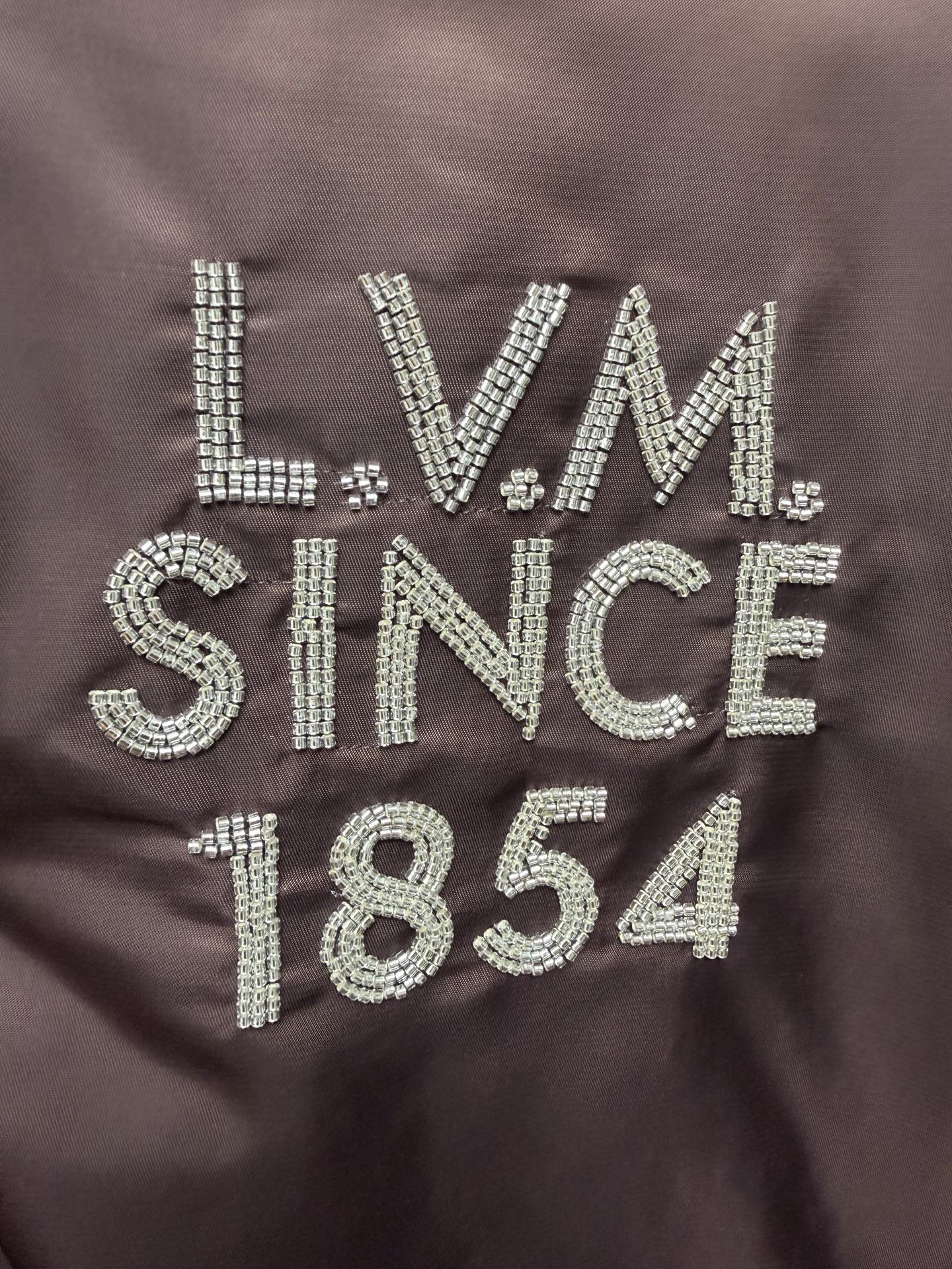 Louis Vuitton long bomber jacket close-up of LVM Since 1854 rhinestone-style logo