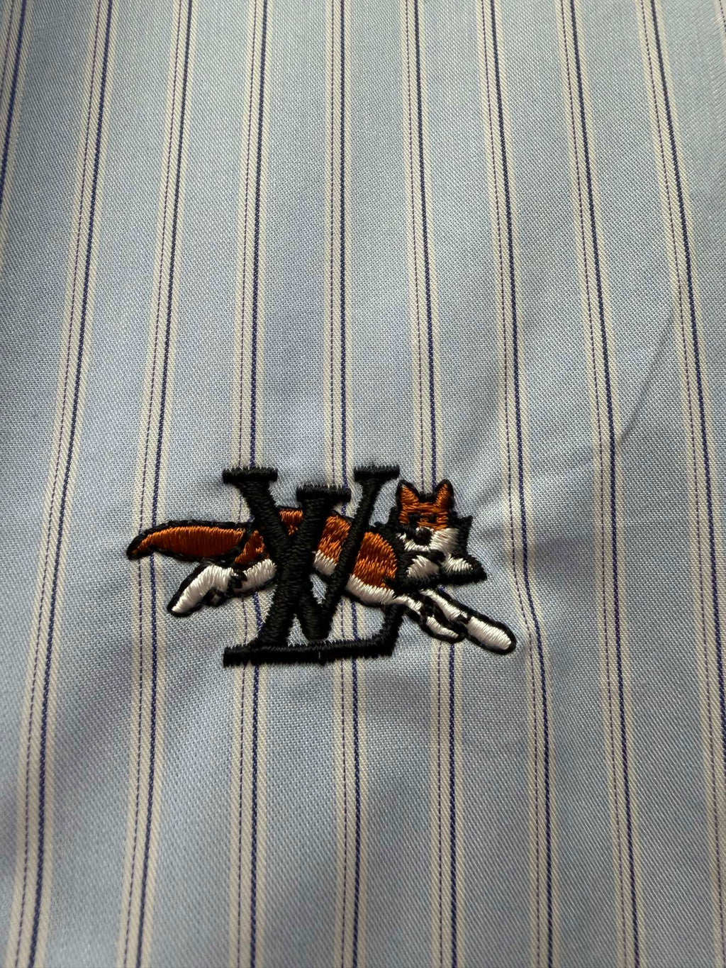 Embroidered logo on light blue striped fabric with black and red accents