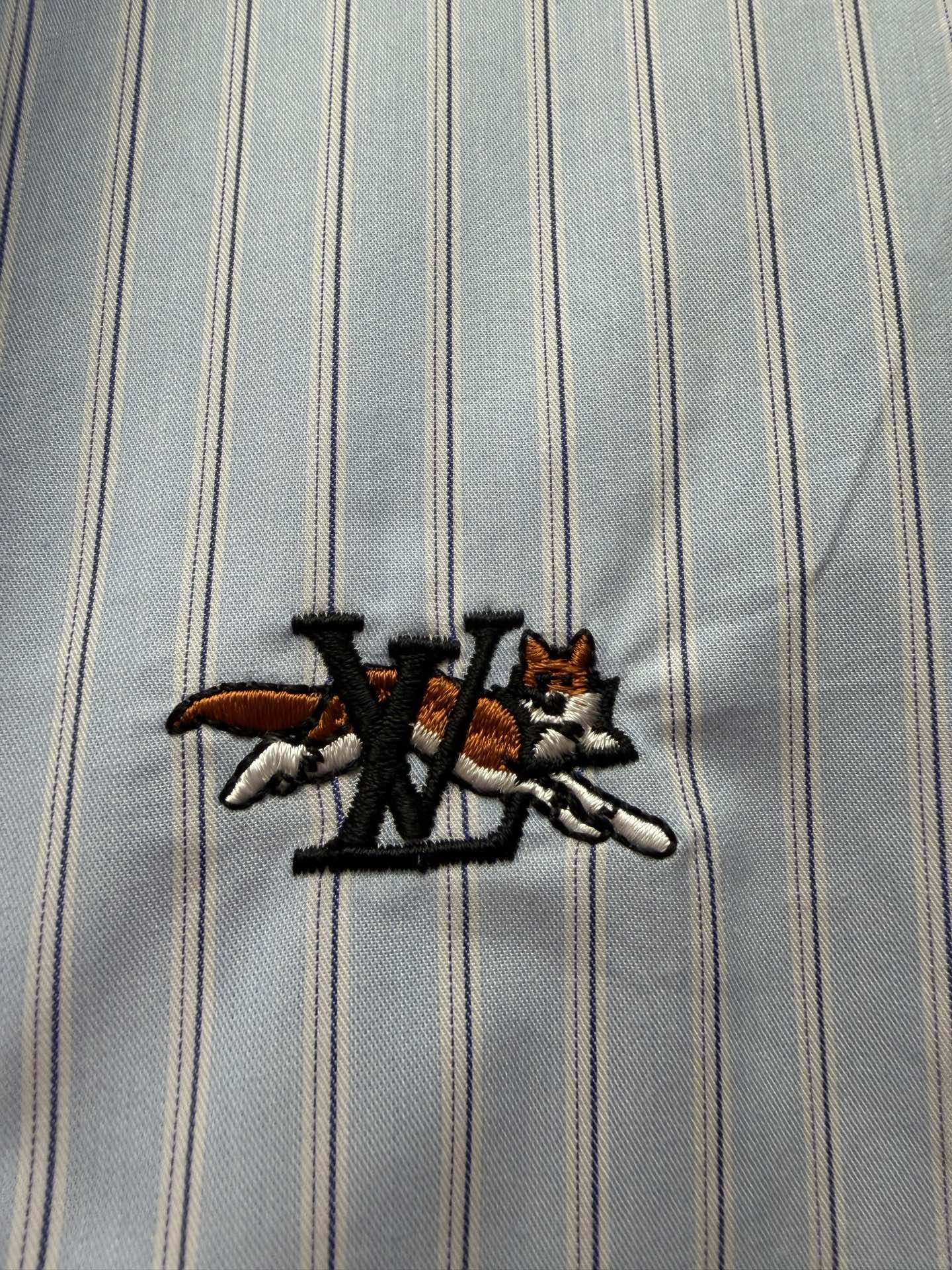 Embroidered logo on light blue striped fabric with black and red accents