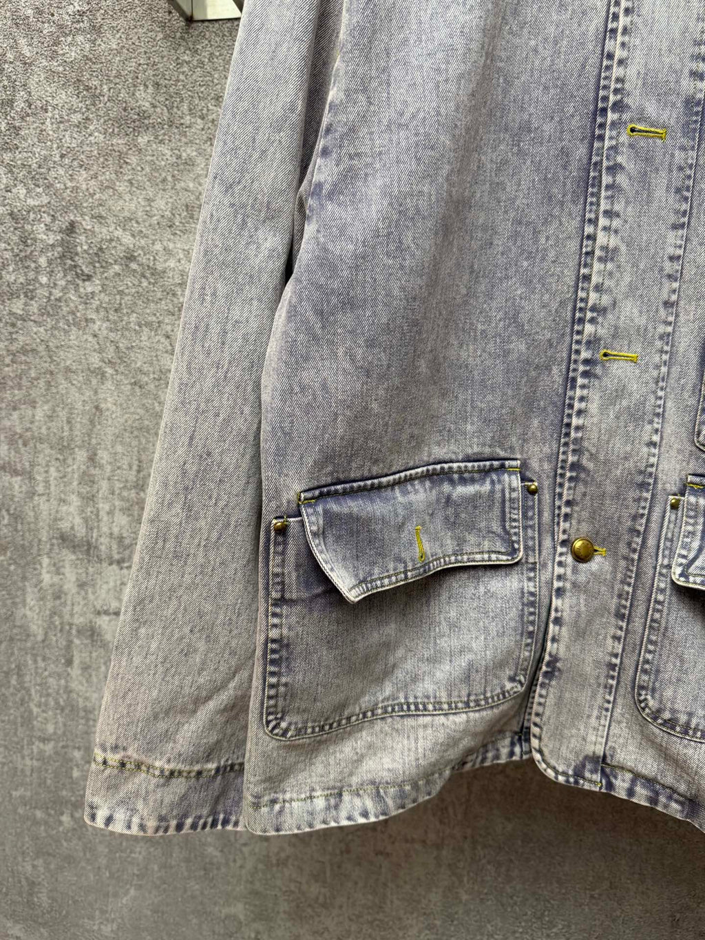 Light blue denim jacket close-up of lower flap pocket with yellow buttons