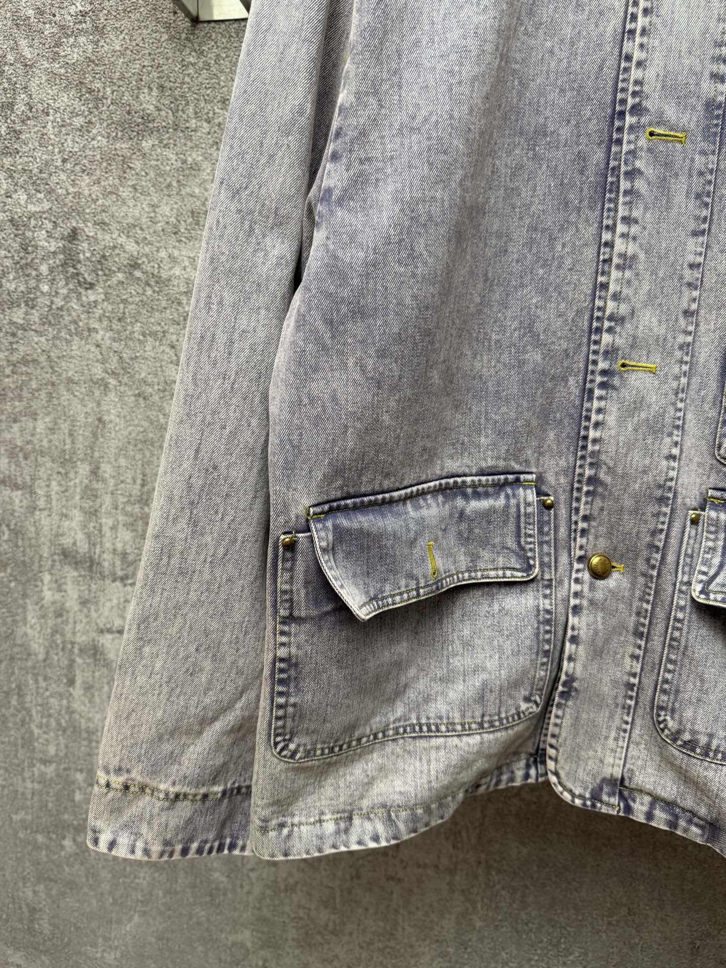 Light blue denim jacket close-up of lower flap pocket with yellow buttons