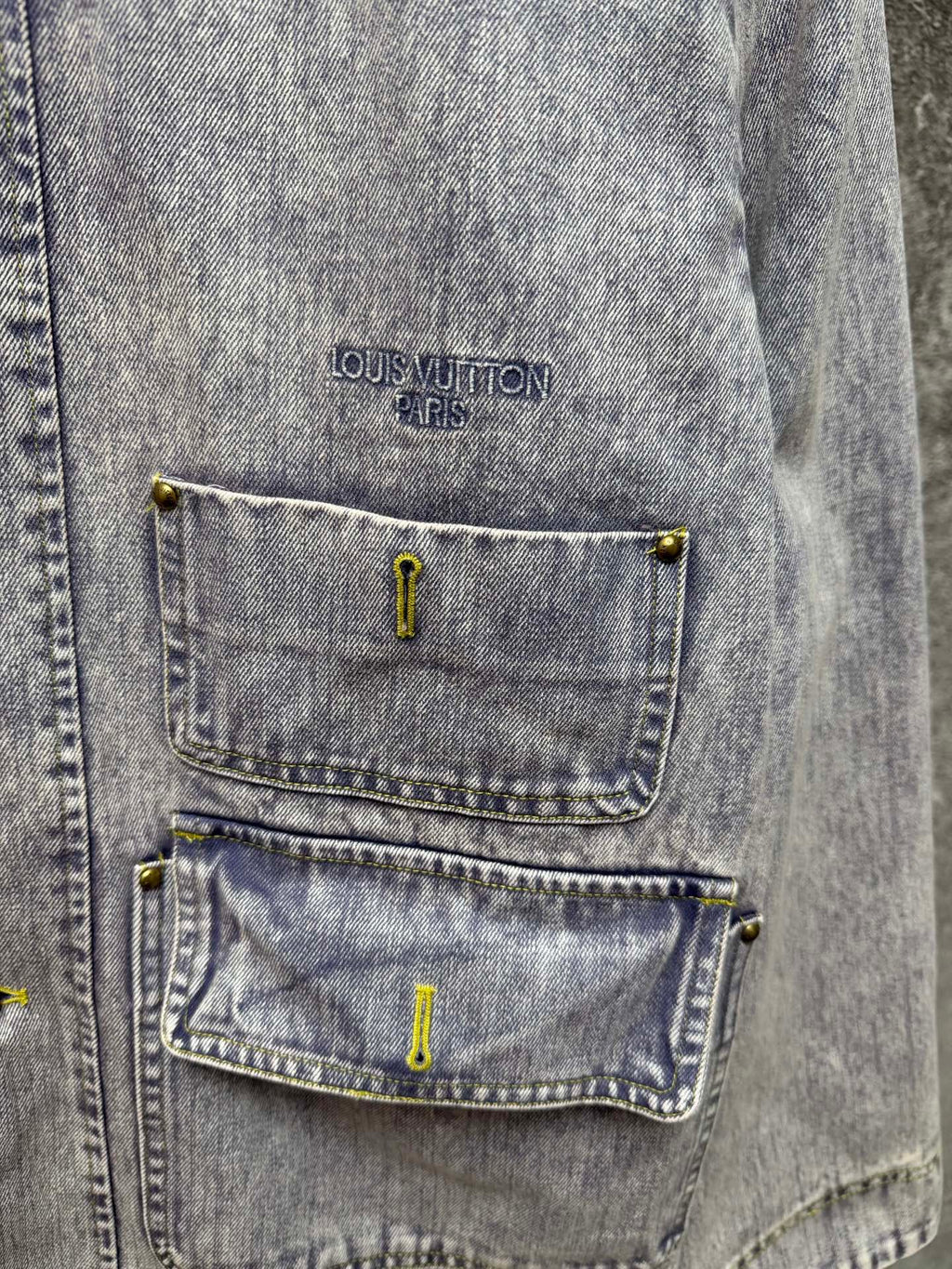 Close-up of light blue denim jacket chest pockets with yellow button accents