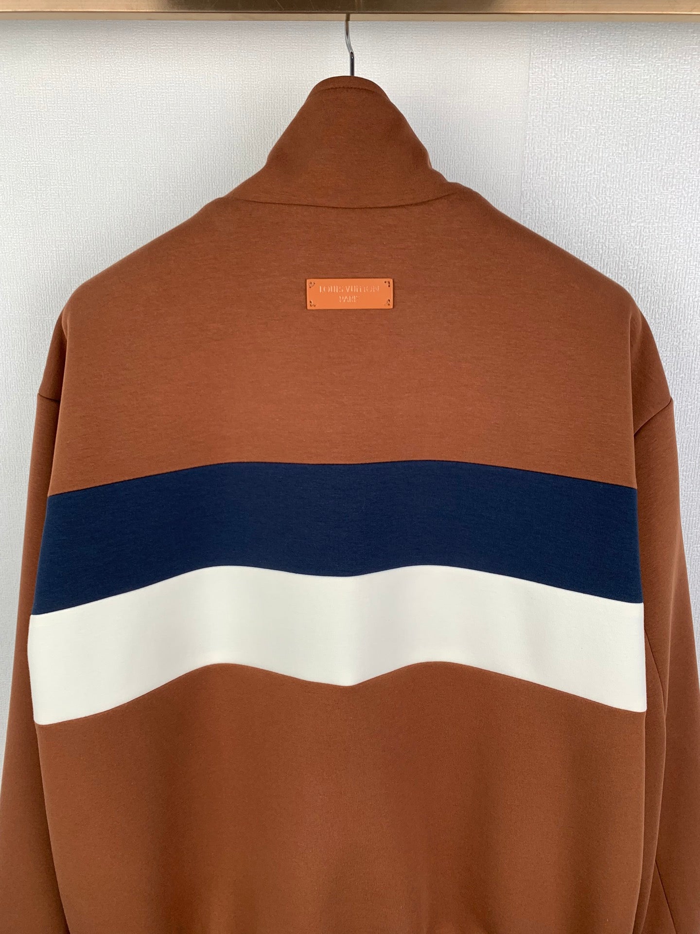 Brown zip-up jacket back with blue and white stripe and small center logo label