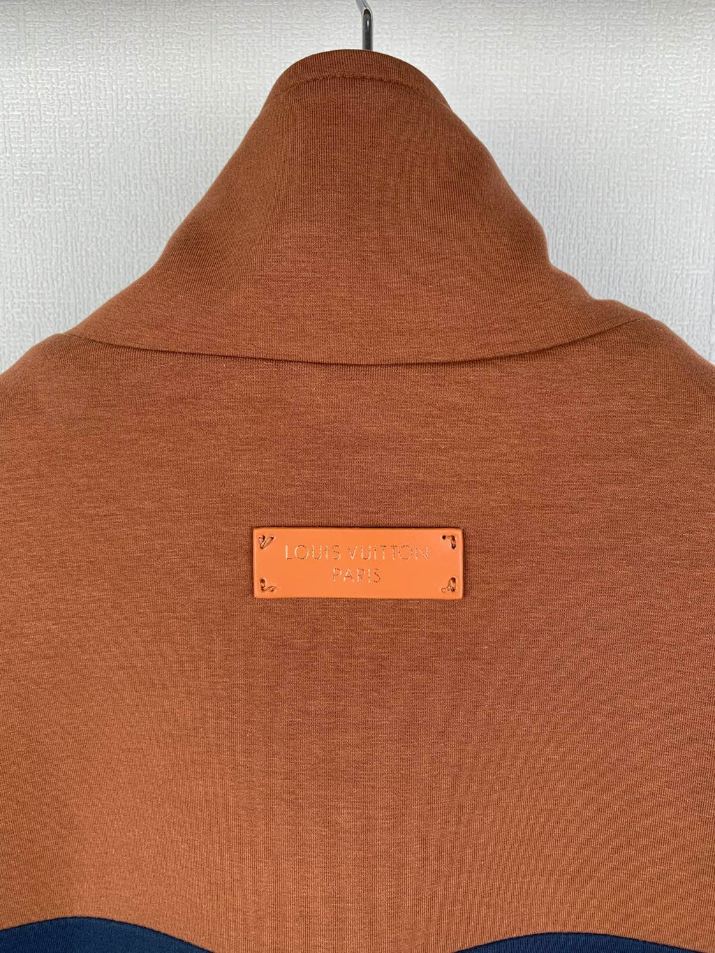 Brown jacket hood and neck area with a small rectangular logo label at center