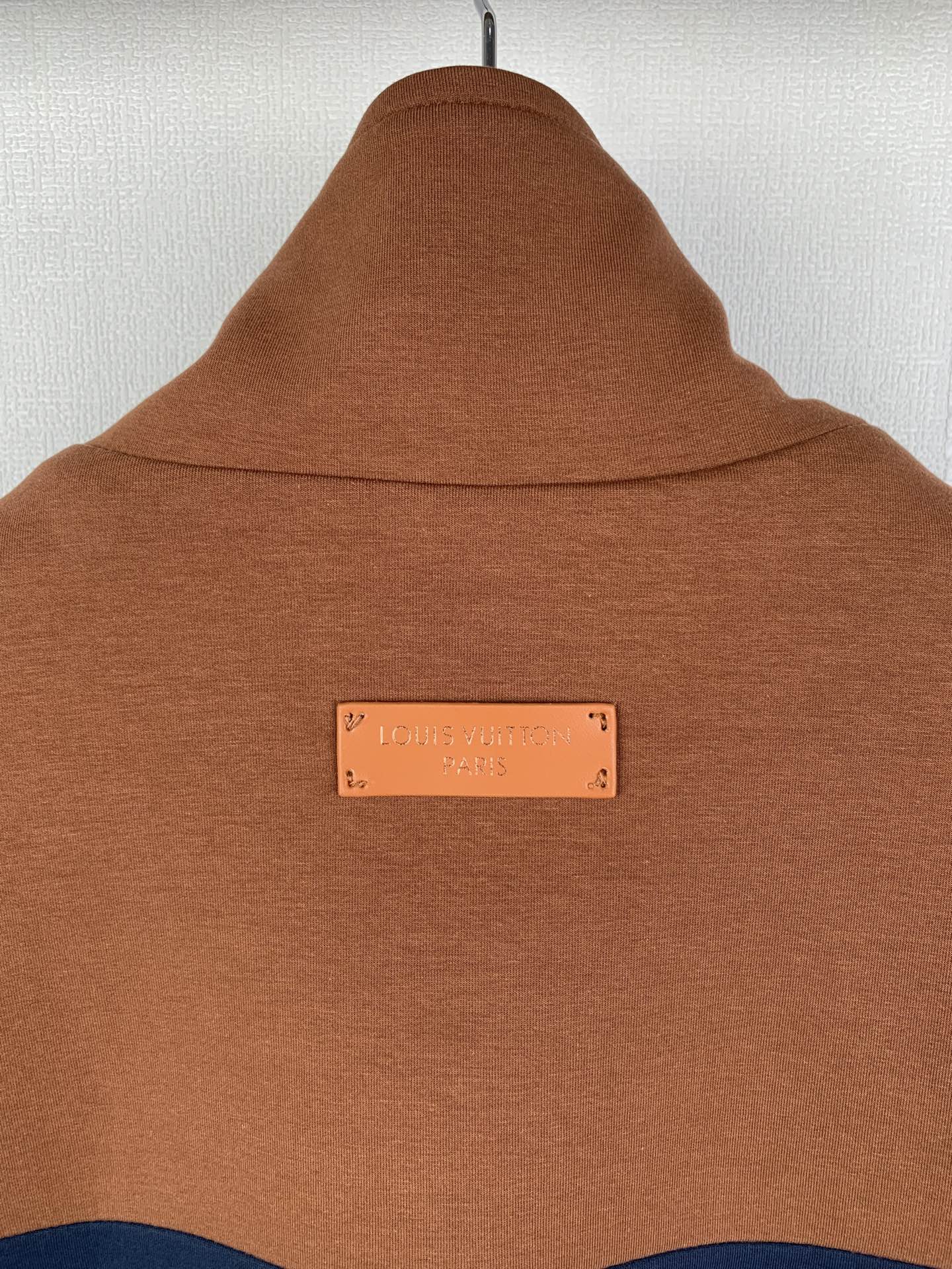 Brown jacket hood and neck area with a small rectangular logo label at center