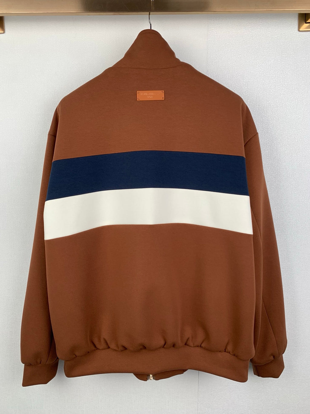 Brown zip-up jacket, back view with blue and white stripe across the torso
