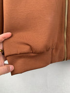 Brown jacket lower cuff with gathered elastic seam; zipper edge visible at side
