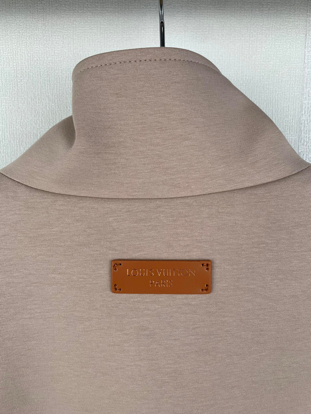 Beige jacket with stand collar and tan logo patch at the neck