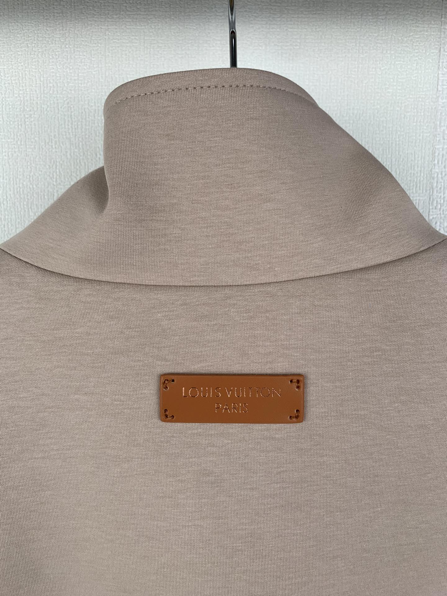 Beige jacket with stand collar and tan logo patch at the neck
