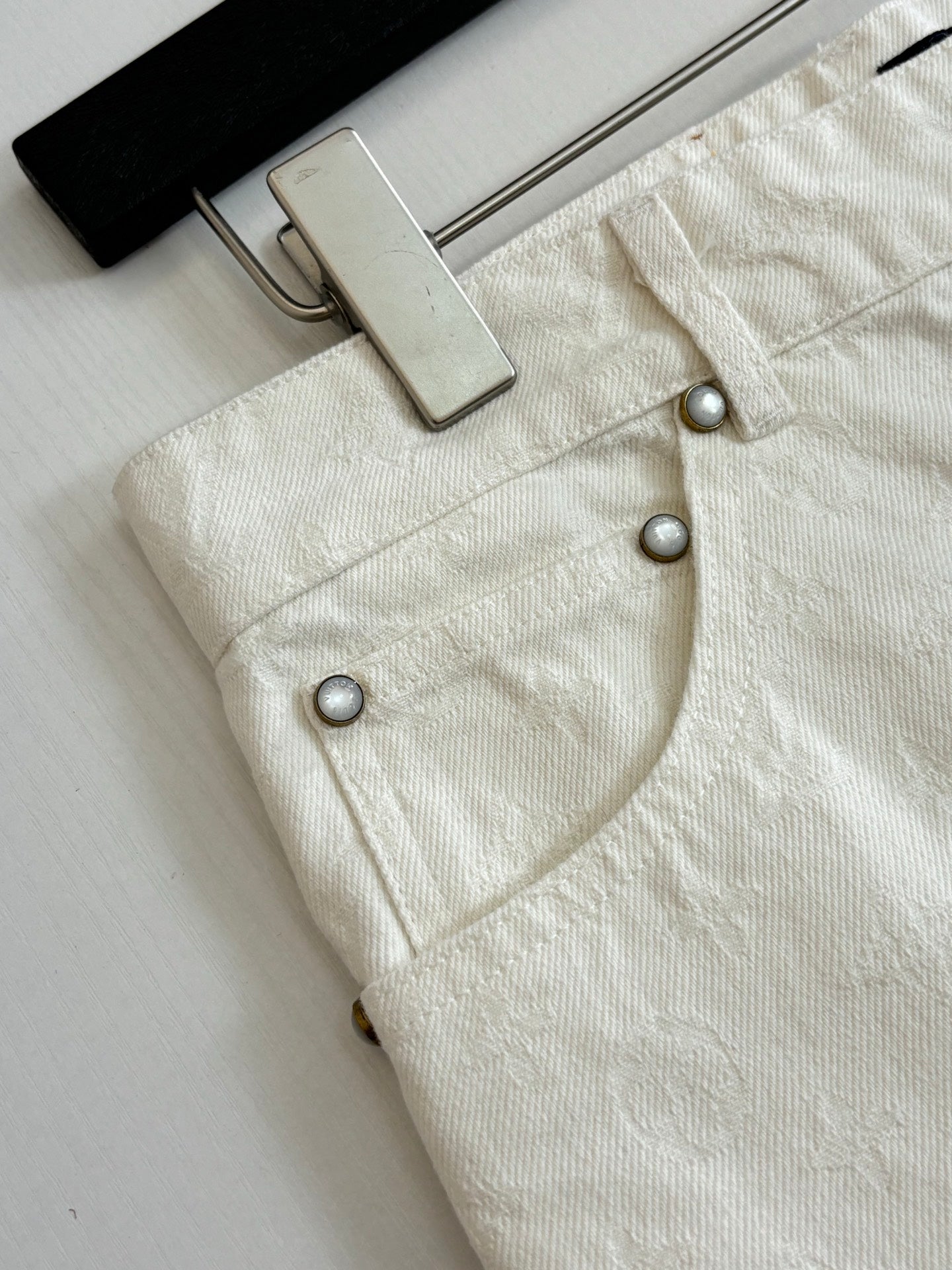 White denim shorts front close-up, metal buttons and waistband hardware