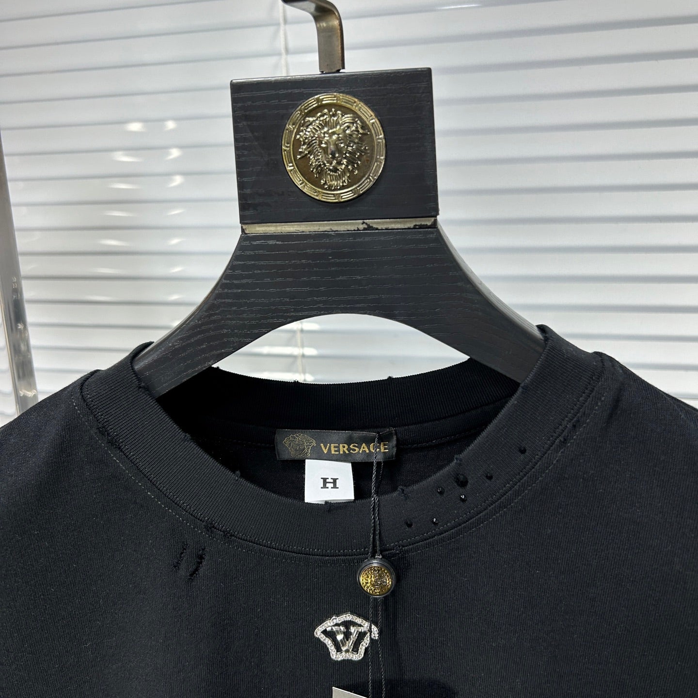 Black crew-neck T-shirt collar with gold pendant charm and small V logo patch