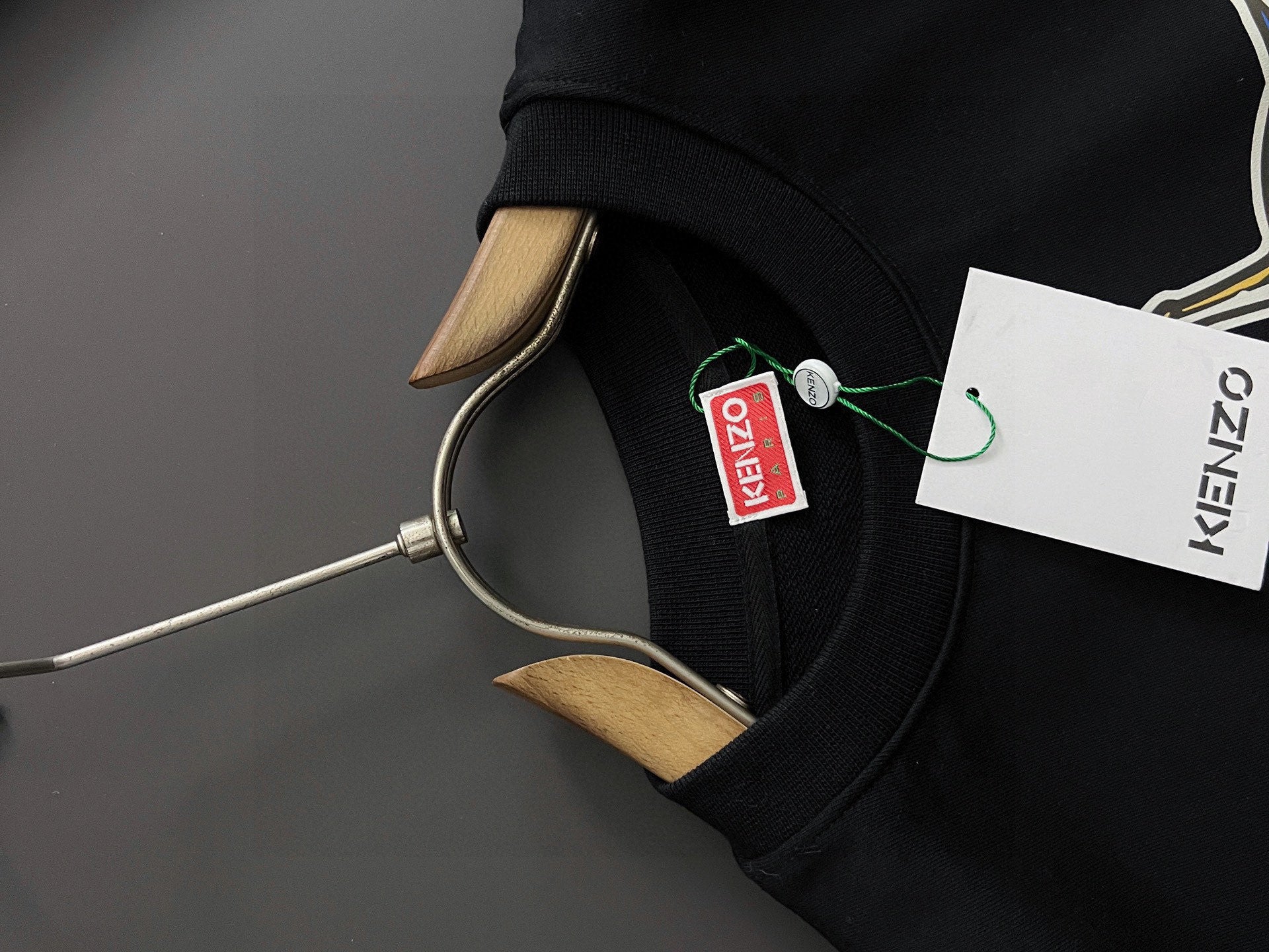 Black sweatshirt sleeve with green and white brand tag near the hem