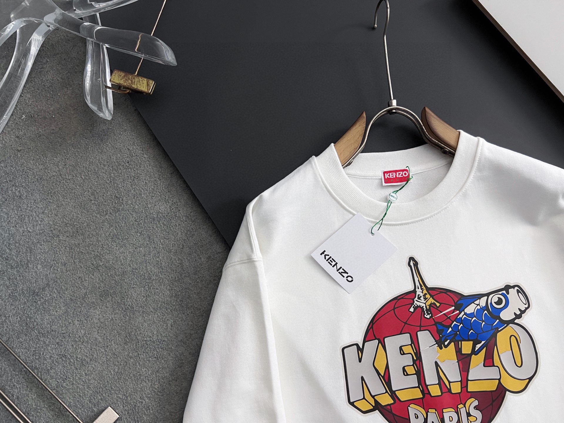 White sweatshirt with Kenzo logo graphic on front, hanging on a wooden hanger
