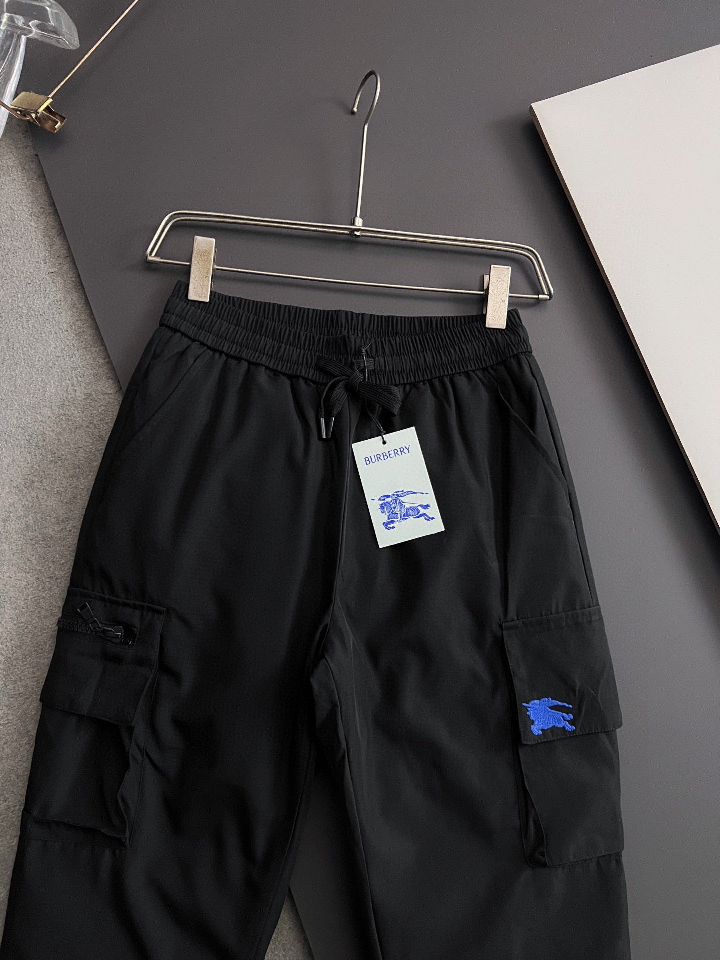 Black cargo pants with elastic waist, drawstring, side pockets and blue patch on thigh