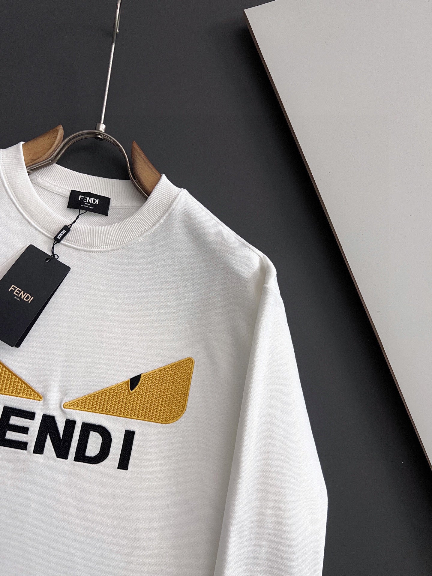 White long-sleeve sweatshirt with yellow V-shaped logo detail and partial FENDI text