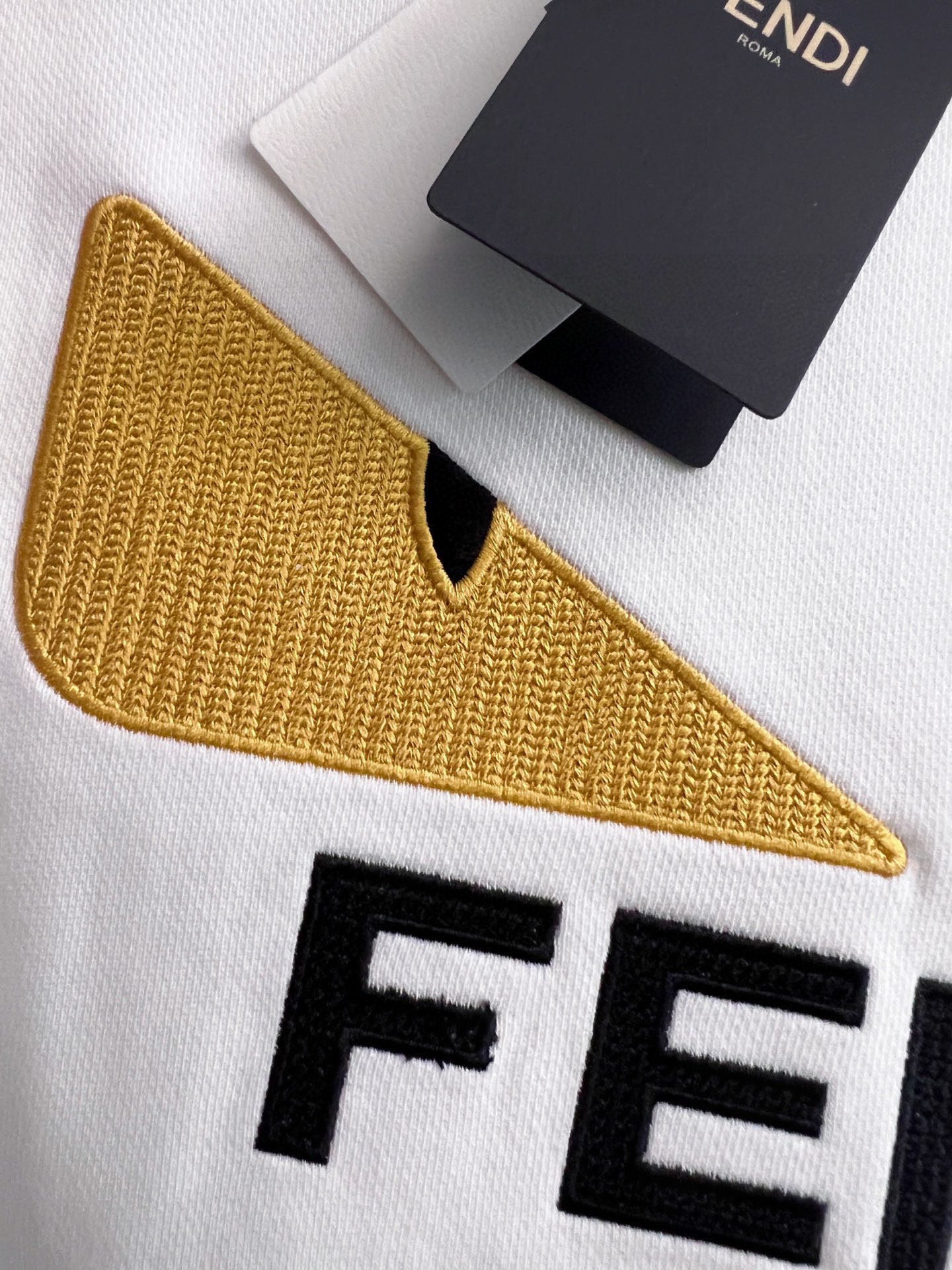 White sweatshirt sleeve with yellow embroidered V detail and black FENDI letters