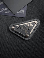 Prada woven logo patch on black fabric, triangular metal-trimmed emblem